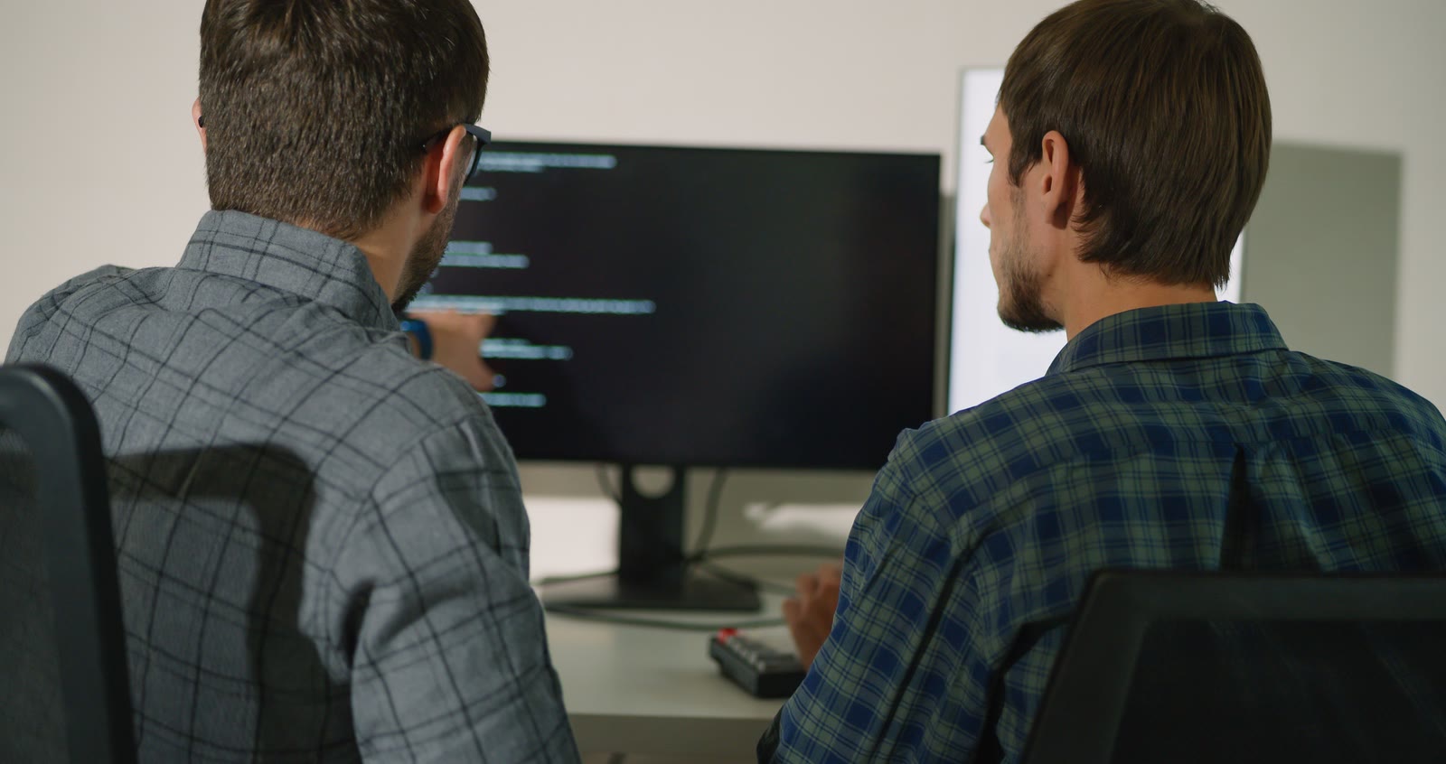 Two people are looking at a computer screen; one of them is pointing to a passage