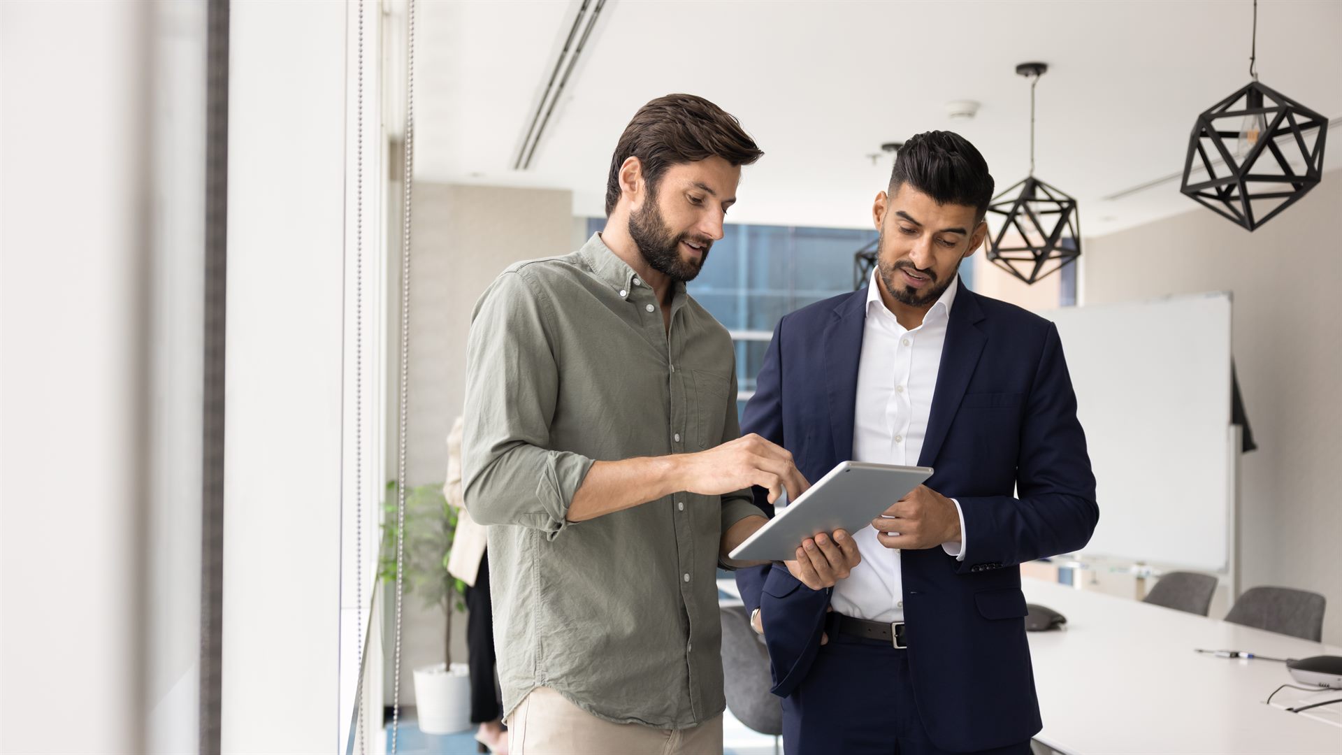 Two people sitting around a tablet in a meeting room, brainstorming ideas