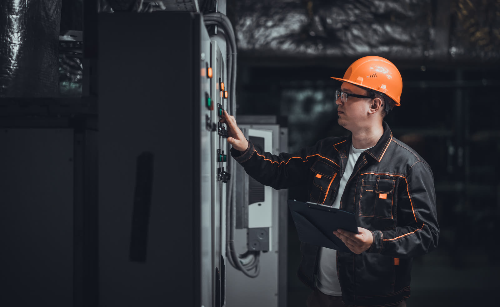 Techniker, der einen industriellen Schaltschrank überprüft, mit einer Notiztafel in der Hand