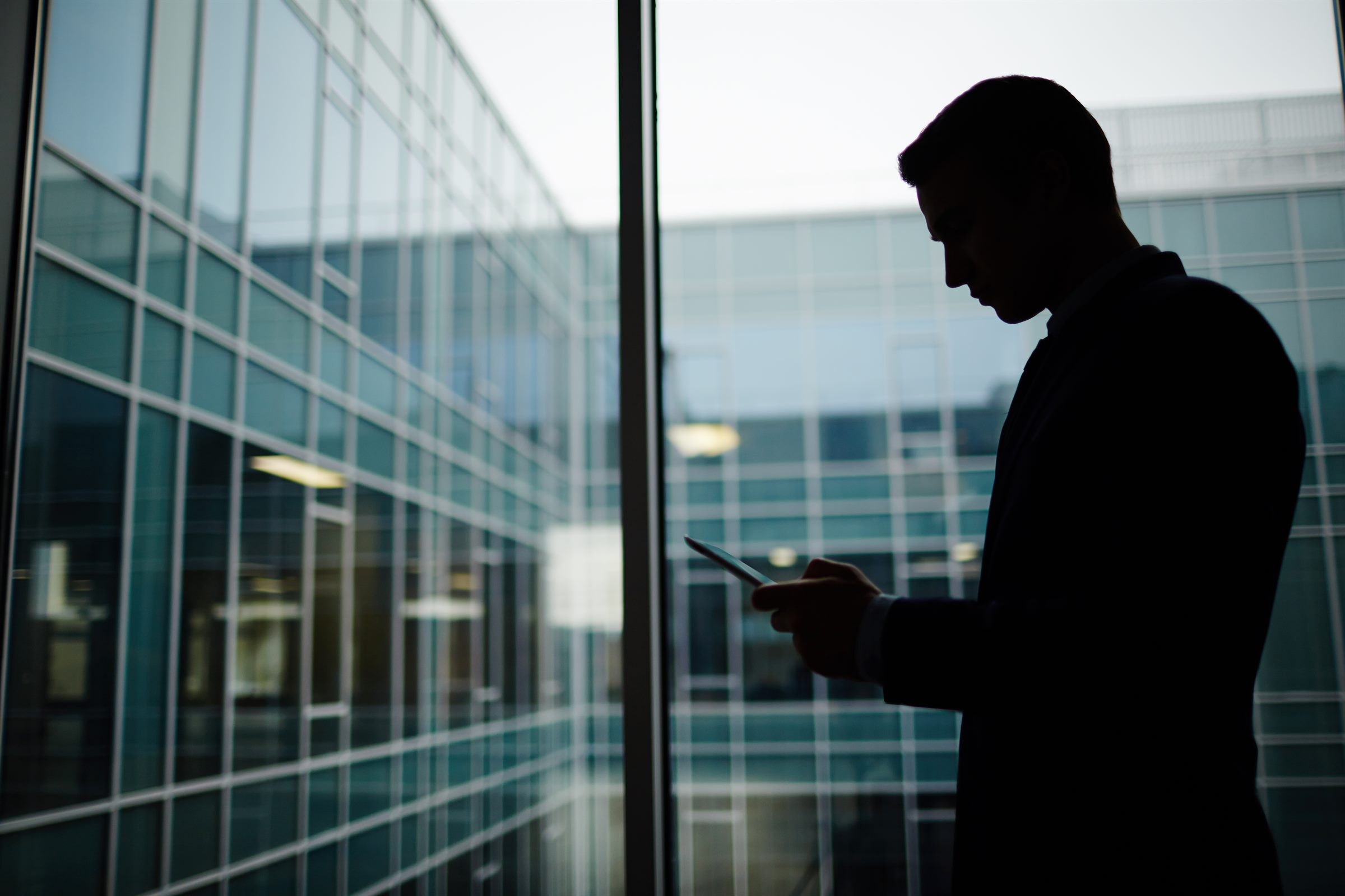 Silhouette d'un conseiller en costume qui lit un message sur son téléphone, devant une façade de bureaux vitrée